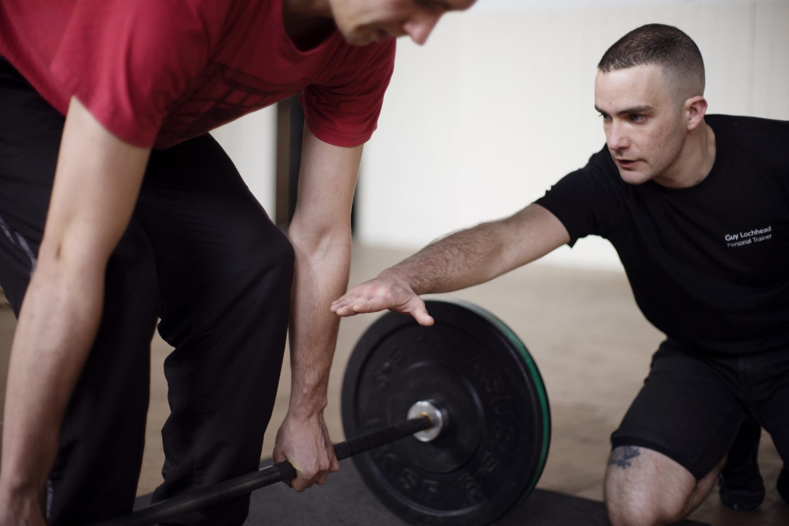 A coach reaching in to cue a lifter's hand position on a loaded barbell.